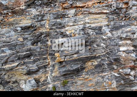 Vue verticale de la formation rocheuse naturelle en couches avec des veines blanches et des pierres fracturées Banque D'Images