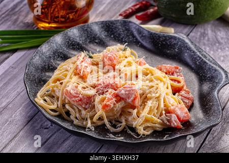 Une délicieuse assiette de spaghettis crémeux avec des morceaux de saumon et du parmesan. Le plat est présenté sur un fond en bois gris rustique avec I frais Banque D'Images