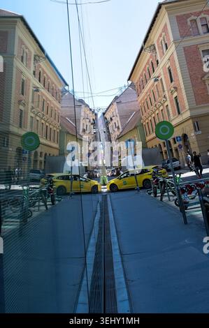 Budapest, Hongrie - 22 mai 2026 : un miroir créatif reflet de la rue Paulay Ede créant une illusion d'optique et une symétrie avec des taxis jaunes. Banque D'Images