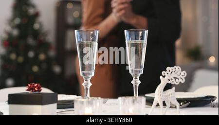 Champagne, noël et cadeau dans la salle à manger de la maison avec couple dansant pour la tradition festive. Alcool, verres et présent sur table dans l'appartement Banque D'Images