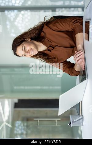 Femme entrepreneure hispanique pensive debout dans le bureau, tenant un dossier avec des documents et prenant une décision ou réfléchissant à une stratégie d'entreprise. Banque D'Images