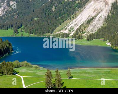 Paysage aérien d'un lac alpin turquoise bordé par une forêt dense, des pentes de montagne escarpées et des prairies verdoyantes, véhiculant la tranquillité, le printemps frais l Banque D'Images