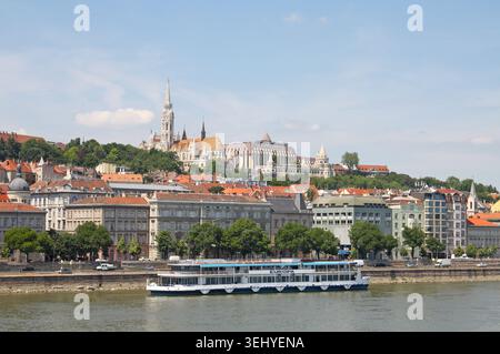 Budapest, Hongrie : vue sur le Danube de Pest à Buda, y compris un bateau de croisière fluviale, le bastion des pêcheurs et l'église Matthias sur la colline du château Banque D'Images