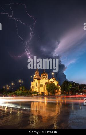 La foudre spectaculaire frappe la cathédrale illuminée de Varna Bulgarie avec des traînées de feux de circulation et un reflet d'asphalte humide Banque D'Images
