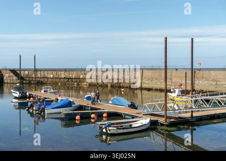 Plusieurs petits bateaux sont amarrés sur des pontons dans un port tranquille de Cairnbulg, Aberdeenshire, Écosse. Trois hommes se tiennent sur un quai comme reflets shimm Banque D'Images
