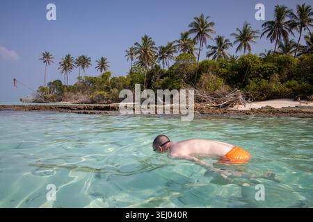 Vashafaru, Maldives - 24 janvier 2026 : vue d'un homme faisant de la plongée en apnée dans une eau turquoise cristalline près d'une île inhabitée avec des palmiers et du blanc Banque D'Images