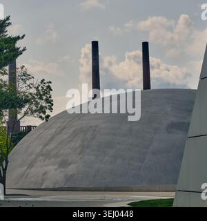 Wolfsburg, Allemagne - 06 juin 2025 : vue de la structure de dôme en béton à Autostadt avec des cheminées industrielles et des arbres sous un ciel nuageux. Banque D'Images