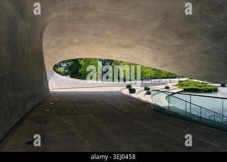 Wolfsburg, Allemagne - 06 juin 2025 : vue sur l'architecture moderne en béton courbé du pavillon Autostadt surplombant des arbres verdoyants et un po tranquille Banque D'Images