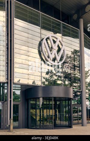 Wolfsburg, Allemagne - 06 juin 2025 : vue du logo Volkswagen sur la façade vitrée du bâtiment Autostadt avec une porte tournante et un arbre Banque D'Images
