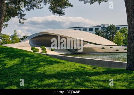 Wolfsburg, Allemagne - 06 juin 2025 : vue du pavillon Porsche moderne d'Autostadt avec son toit en béton incurvé, sa pelouse verte et son étang réfléchissant. Banque D'Images