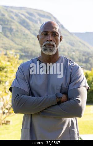 Homme afro-américain senior debout les bras croisés à l'extérieur dans la cour portant des maquillages gris et une montre Banque D'Images