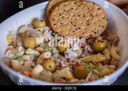 Salade de thon avec laitue, mayonnaise et olives farcies, garnie de craquelins de sésame dans un bol blanc, vue en angle, image en gros plan Banque D'Images