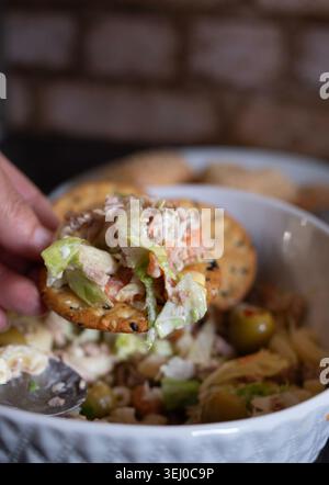Main prendre un craquelin de sésame pour servir une salade de thon comme apéritif lors d'un repas de famille, image verticale en gros plan Banque D'Images