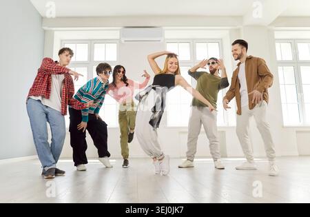 Groupe de jeunes amis joyeux et heureux excités hommes et femmes s'amusant ensemble dansant à l'intérieur. Banque D'Images