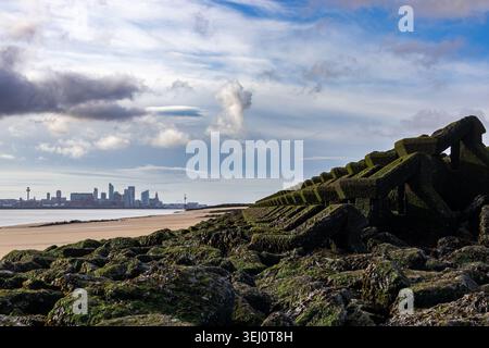 Armure rocheuse recouverte d'algues et mur de mer sur la plage de New Brighton avec les gratte-ciel de Liverpool sur la rivière Mersey sous ciel nuageux Banque D'Images