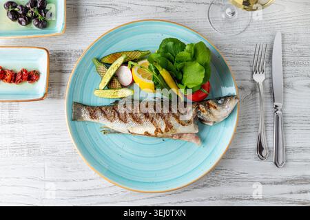 Bar grillé avec laitue, citron, maïs bébé et légumes frais sur assiette bleue Banque D'Images