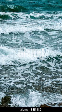Les vagues de l'océan s'écrasent sur la plage de sable avec du surf blanc mousseux et de l'eau turquoise créant une scène côtière dynamique dans des conditions d'éclairage naturel Banque D'Images