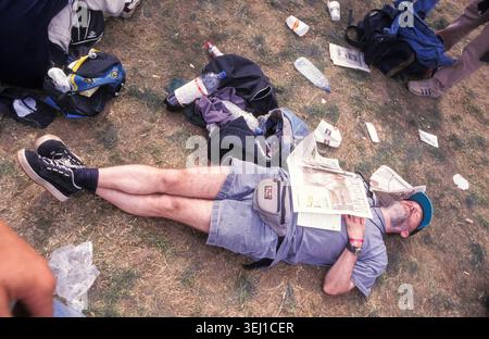FANS DE ROCK et FANS DE MÉTAL, READING FESTIVAL, 1997 : un homme est endormi complètement hors de lui sur l'herbe parmi la litière d'un festival, un journal sur sa poitrine. Une scène franche du site et de la foule dans la zone de main Stage Arena au Reading Festival 1997 du 1997 août à Reading, Angleterre Royaume-Uni. Photo : Rob Watkins Banque D'Images