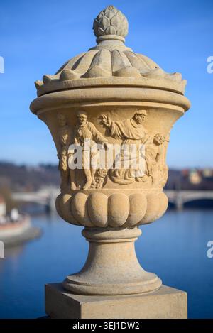 Vue rapprochée d'une urne en pierre sculptée avec des figures humaines sur un pont, sur un ciel bleu et un fond de rivière doux en plein jour Banque D'Images