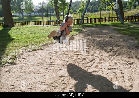 Enfant joyeux s'amusant sur une balançoire de piste de câble dans un parc d'été. Banque D'Images