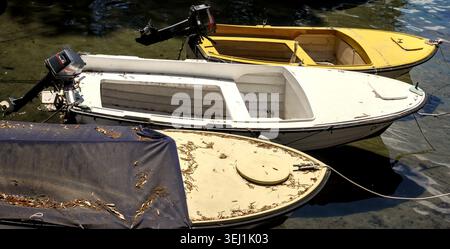 Petits bateaux à moteur hors-bord amarrés ensemble sur la surface de l'eau calme près de la côte à Opatija, en Croatie, couverts de feuilles mortes et de brindilles. Banque D'Images