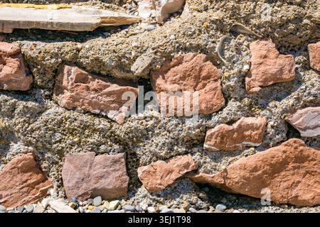 Une vue rapprochée d'un mur de pierre texturé fait de diverses pierres brun rougeâtre et de mortier. La surface montre des imperfections naturelles et des tons terreux. Banque D'Images