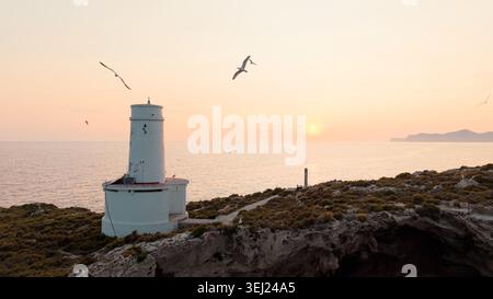 Vieux phare sur la côte rocheuse avec mouettes volantes au beau coucher de soleil Banque D'Images