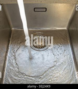 Gros plan de l'eau fraîche s'écoulant d'un robinet de cuisine dans un évier en acier inoxydable Banque D'Images
