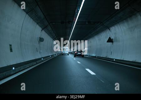 Un point de vue à angle bas pris à partir d'un véhicule en mouvement à l'intérieur d'un tunnel routier moderne en béton, montrant la circulation devant, les marquages de voie réfléchissants et le brick Banque D'Images