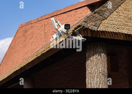 Caméra de sécurité avec antenne montée sur le bord du toit de chaume rustique avec des piliers de support en bois. Système et technologie de surveillance CCTV Banque D'Images