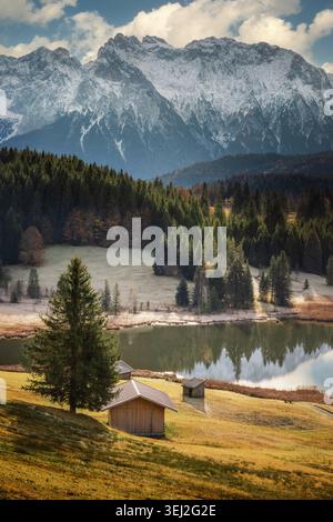 Paysage peint sur un lac dans les Alpes allemandes, avec des montagnes et des cabanes sur une prairie jaune au soleil Banque D'Images