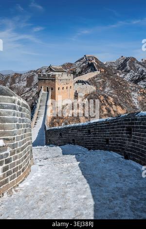 Enneigée de la Grande Muraille de Jinshanling serpentant à travers les montagnes sous un ciel bleu clair d'hiver. Banque D'Images