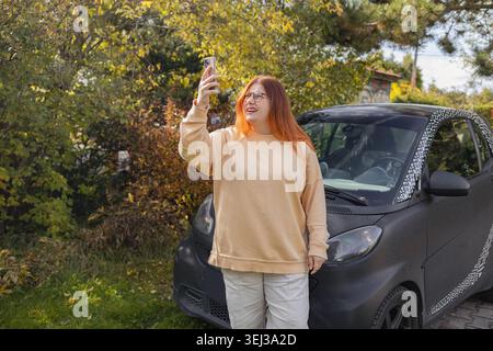 Femme essayant de trouver le signal de téléphone portable près de la voiture. Femme heureuse prenant selfie près de la voiture sur le Road trip Banque D'Images