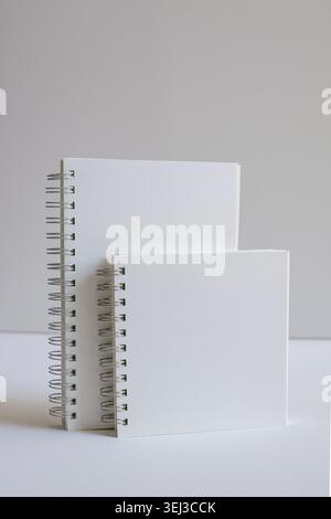 Cahiers à spirale debout affichés sur la surface blanche dans le studio. Papeterie minimale, image de marque moderne, espace de travail créatif, organisation élégante, propre Banque D'Images