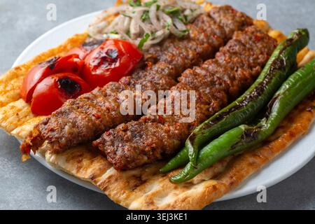 Adana Kebab traditionnel turc servi sur du pain plat avec des légumes grillés et une salade d'oignons Banque D'Images