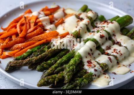 Vue latérale d'asperges vertes rôties et de carottes avec sauce crémeuse et piments Banque D'Images