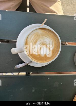Une vue de dessus directe d'une tasse en céramique blanche remplie d'un cappuccino chaud montrant un magnifique design d'art latte en forme de coeur sur une table en bois. Banque D'Images