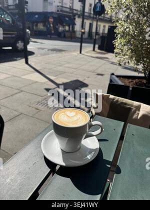 Une tasse en céramique blanche de cappuccino chaud avec un magnifique motif de coeur de latte art assis sur une table de terrasse en bois vert foncé dans un café en plein air à Londres Banque D'Images
