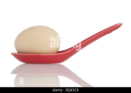 Oeuf brun dans une cuillère en céramique rouge isolé sur fond blanc Banque D'Images