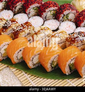 Nourriture, rouleaux de sushi colorés sont disposés soigneusement sur un tapis de bambou. Différents types de saumon sont composés de saumon frais, de légumes croquants et de sauces savoureuses. Parfait Banque D'Images