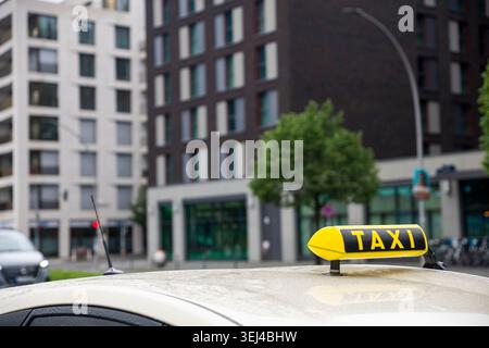 Gros plan sur un panneau de taxi jaune monté sur le toit d'une voiture de couleur crème couverte de gouttes de pluie. Le panneau a le mot 'TAXI' écrit i. Banque D'Images