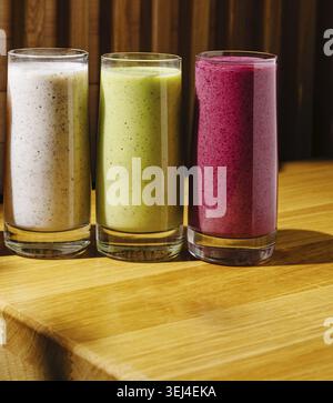 Nourriture, trois smoothies colorés assis dans de grands verres sur une surface en bois. Les boissons présentent des textures crémeuses et des couleurs vives, mettant en valeur un délicieux Banque D'Images