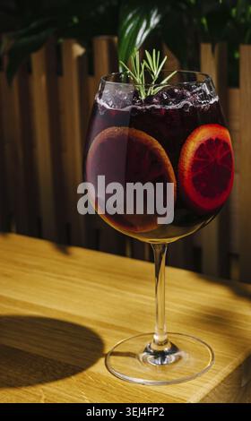 Nourriture, Un cocktail coloré se trouve élégamment sur une table en bois, mettant en vedette des tranches d'orange sanguine et un brin d'herbe verte. La boisson scintille au soleil Banque D'Images