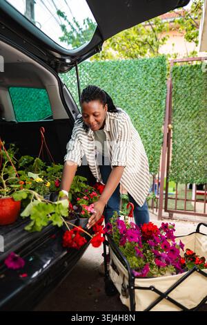 Femme chargeant des fleurs colorées dans le coffre de voiture pour le jardinage Banque D'Images
