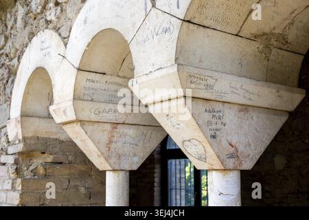 Vieste - Pouilles - Italie - 29 août 2025 : détail d'arches et de colonnes en pierre pâle recouvertes de graffitis manuscrits et de noms rayés, avec une porte sombre Banque D'Images