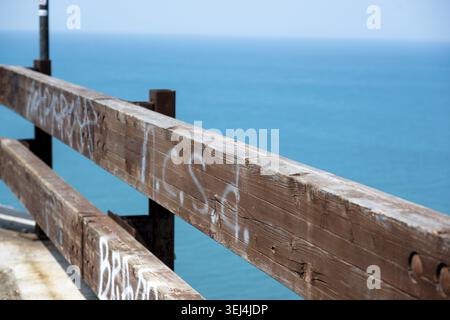 Vieste - Pouilles - Italie - 08-29-2025 : gros plan d'une balustrade en bois altérée avec des graffitis décolorés, avec de l'eau de mer turquoise claire et un lointain poil Banque D'Images