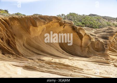 Falaises de grès érodées façonnées par le vent près de Portu Maga, Sardaigne, avec des textures en couches, des dunes sèches, une végétation clairsemée, et ciel bleu Banque D'Images
