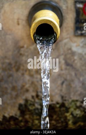 Gros plan d'un ruisseau d'eau s'écoulant d'une fontaine en pierre antique contre un mur altéré Banque D'Images