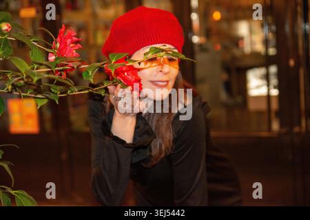 Femme en béret rouge sentant des fleurs de camélia rouges la nuit Banque D'Images