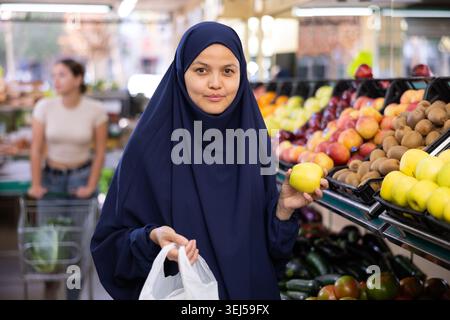 Une jeune femme du hijab achète des pommes à l'épicerie Banque D'Images